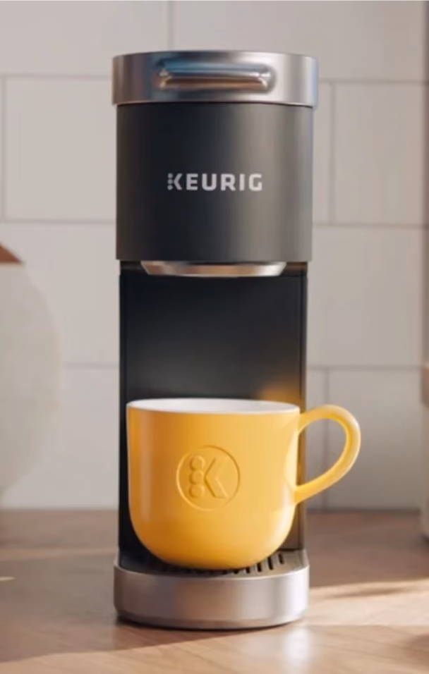 Keurig coffee machine with a yellow mug placed on the drip tray on a wooden surface.
