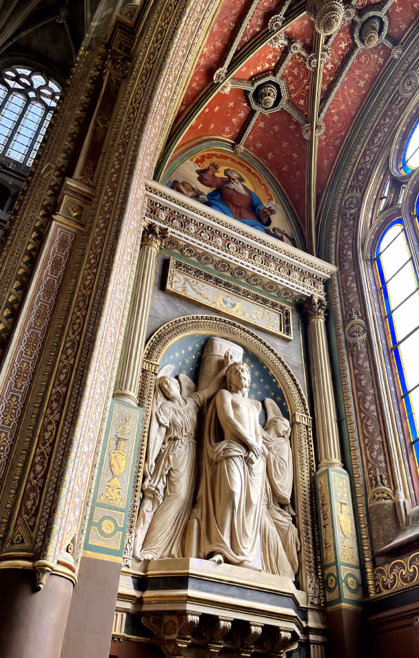 Ornate church interior with carved stone figure and detailed red vaulted ceiling above stained glass windows.